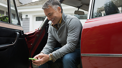 A man sitting in a red car while smiling down at a green phone in his hands 