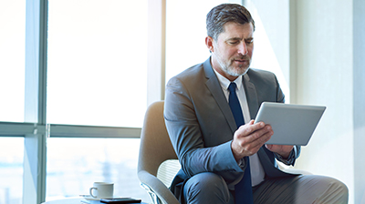 Man in business attire sitting and using a tablet.
