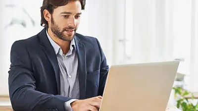 Man in business attire sitting and using a laptop.