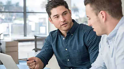Two men speaking to each other while looking at a laptop 