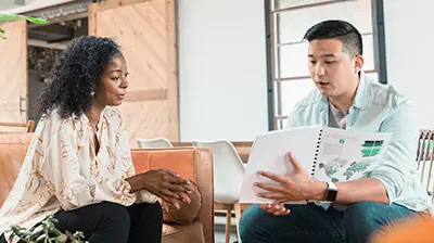 A man sitting next to a woman while showing her something in a booklet that he is holding