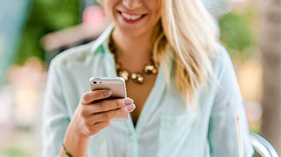 Woman in casual clothes, smiling while looking down at mobile phone in her hand. 