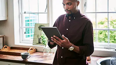 A man standing in his kitchen while holding a tablet 