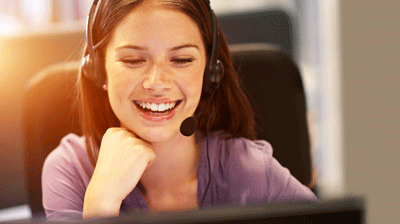 A woman wearing a headset while smiling with her hand rested under her chin 