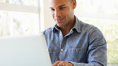 A man in a jean button down shirt typing on his laptop 