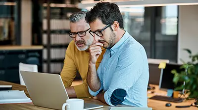 Two men, both wearing glasses, looking intently at a laptop screen