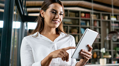 A woman in a white blouse smiling and pointing at a tablet in her hand. 