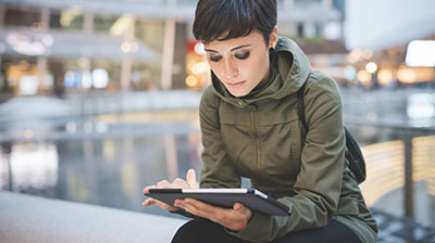 Woman in casual attire sitting on an bench, while looking down at a mobile phone in her hands.
