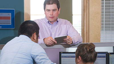 A man interacting with two coworkers at a work station
