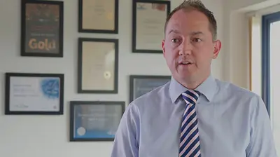 A man in a tie standing in front of a number of awards