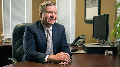 Man dressed in business attire sitting in office smiling and looking forward.