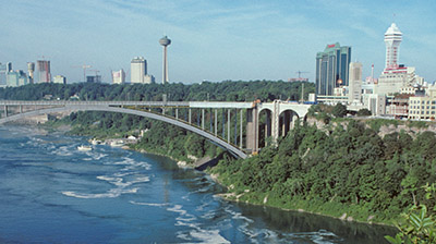 View of a bridge going across a river with a city skyline in the background 
