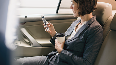 Businesswoman in car holding coffee reading her smart phone