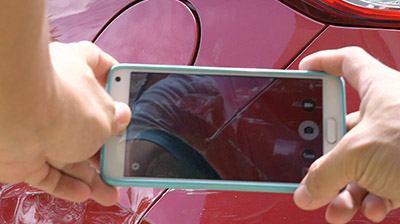 Two hands holding a phone while taking a picture of a red car 