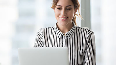 A woman in a striped blouse smiling at her open laptop 