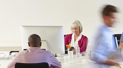 A few people working in an office. A businesswoman at her desk is the focal point