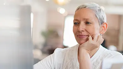 Woman in casual attire using a desktop computer  and smiling.