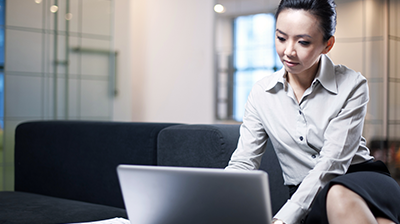 Woman in business attire sitting in office lobby while working on her laptop