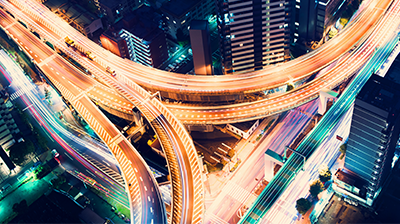 Busy intersection near tall buildings at night with light trails