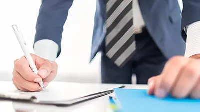 A businessman leaning over a desk writing on paper