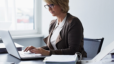 Woman in business casual attire sitting at desk using laptop.
