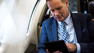 Man in business attire sitting on an airplane using a tablet.