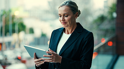 Woman in business attire standing outside using a tablet.