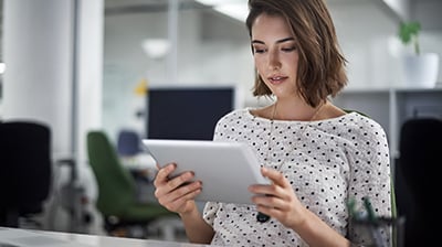 Woman in business casual attire sitting at desk using a tablet.