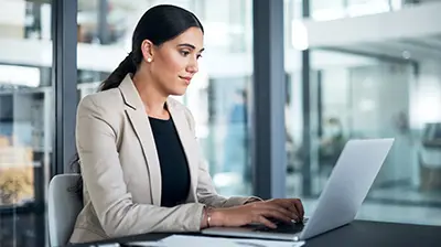 Woman dressed in business attire sitting at a table using a laptop.