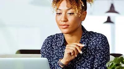 A woman in a blue blouse, looking at her laptop 