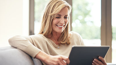 A woman sitting on a chair, smiling while using her tablet 