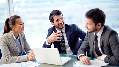 Two men and a woman in business attire having a meeting with a laptop and paper on the table